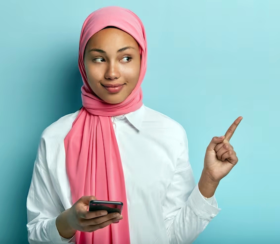 satisfied-good-looking-female-with-dark-skin-holds-cell-phone-chats-with-followers-social-networks-points-away-fore-finger-demonstrates-free-space-promotional-content-wears-scarf-head_273609-26740